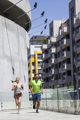 Fototapeta premium Handsome man and beautiful woman jogging together on street between residential buildings