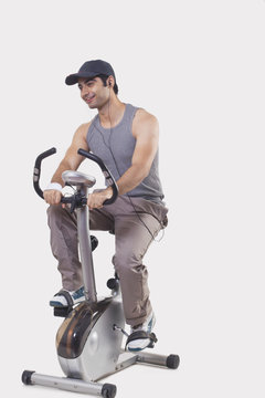 Young man listening music while exercising over white background 
