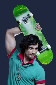 Young man posing with skateboard against black background 