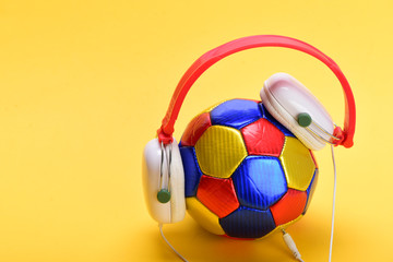 Modern earphones and football isolated on light orange background