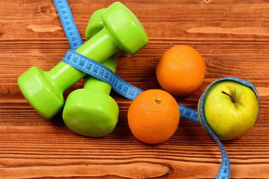 green dumbbells weight with measuring tape and apple, orange
