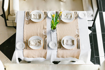 Stylish, white dining festive table and sofas. Minimalist interior in monochrome. Black and white concept. Wedding preparation. Empty restaurant top view.