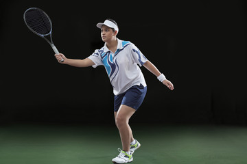 Fototapeta na wymiar Young female player in sportswear playing tennis over black background