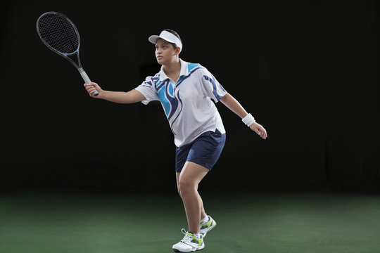 Young female player in sportswear playing tennis over black background