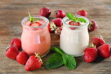 Jars with delicious homemade yogurt and strawberry on wooden table