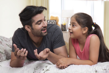 Father and daughter lying on bed and talking