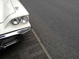 Amerikanischer Sportwagen der Fünfzigerjahre in Weiß mit Doppelscheinwerfer auf grauem Asphalt...