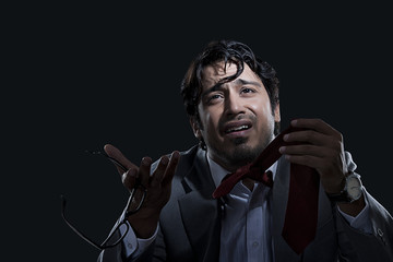 Irritated young businessman holding glasses and tie over black background