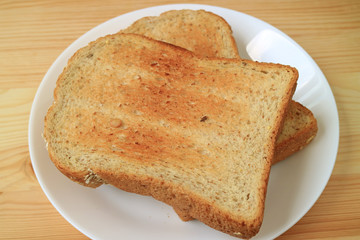 Two pieces of whole wheat toast served on ceramic white plate on wooden table 