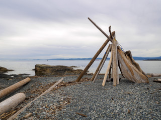 Driftwood Teepee (tipi) structure on a rock pebble beach by the water on the coastline