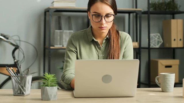 Young attractive brunette woman working with laptop computer in modern urban office. Woman typing on keyboard, reading, surfing inernet. Close up