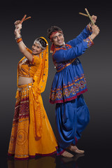 Fototapeta premium Full length portrait of happy young Indian couple performing Dandiya Raas over black background