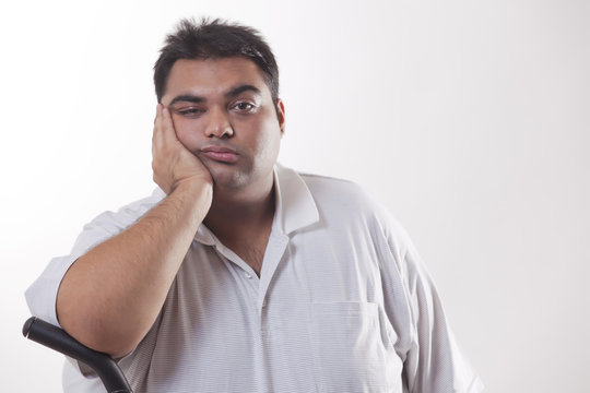 Portrait of a tired obese man with hand on face over white background 