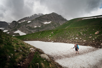Tourist with a large backpack on the pathway in the background of high snow-capped mountains