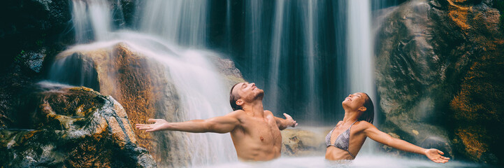 Nature couple relaxing under waterfall with open arms in freedom banner. People enjoying water...