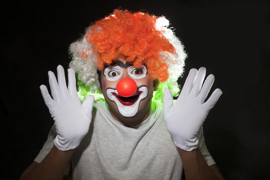 Close-up of male clown performing over black background 