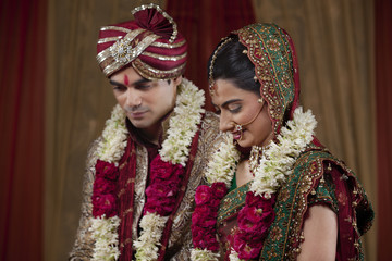 Young couple wearing garlands looking down 