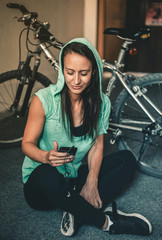 Young woman with a hoodie resting after workout, listening to music