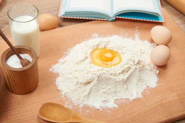 Flour and broken egg closeup for baking on a wooden background. Raw food and kitchen utensils.