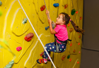 little girl in a pink T-shirt climbing a rock wall indoor