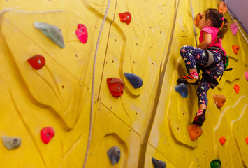 little girl in a pink T-shirt climbing a rock wall indoor