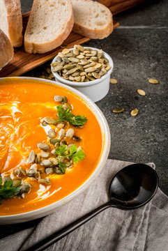 Traditional fall and winter dishes, hot and spicy pumpkin  soup with pumpkin seeds, cream and freshly baked baguette, on black stone table, copy space