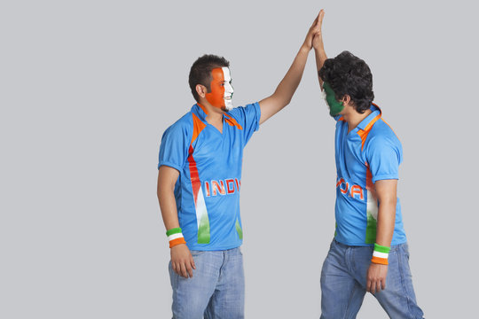 Male cricket fans in jerseys giving a high-five to each other over colored background 