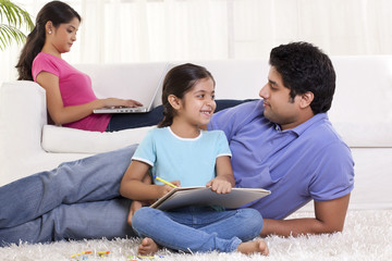 Father and daughter looking at each other while mother using laptop in the background 