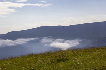 Горный пейзаж, туман в горном ущелье, белые облака над склонами, дикая природа