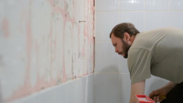 The worker removes the old ceramic tile from the wall in the bathroom