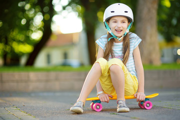 Pretty little girl learning to skateboard on beautiful summer day in a park. Child enjoying skateboarding ride outdoors.