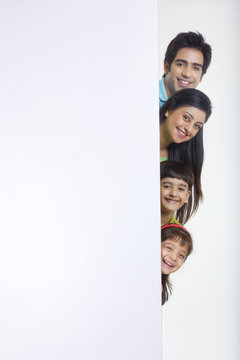 Portrait Of Family Peeking Behind White Board