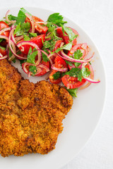 fried beef schnitzel with salad of tomatoes, red onion, and parsley 