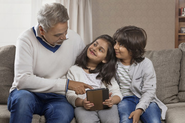 Happy grandfather and grandchildren using digital tablet	