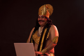 Man dressed as Raavan working on a laptop 