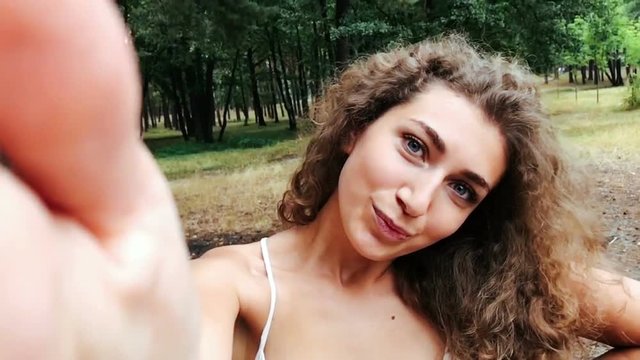 Young woman with curly hair posing for smartphone for selfie