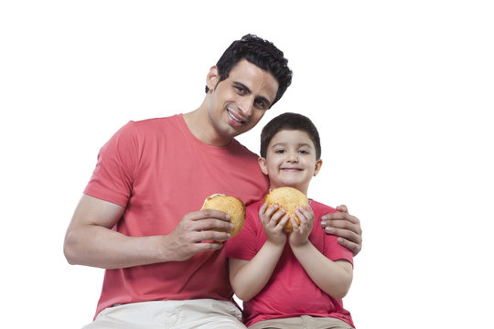 Portrait of happy father and son holding burgers over white background