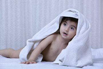 Little boy with a towel on his head on a bed 