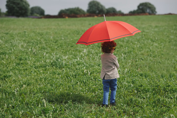 little boy with red umbrella in summer field