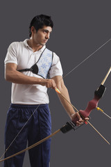 Young male archer with bow and arrow isolated over gray background