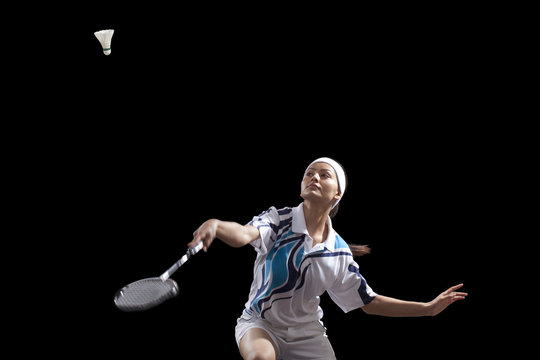 Woman Hitting Shuttlecock With Badminton Racket Isolated Over Black Background