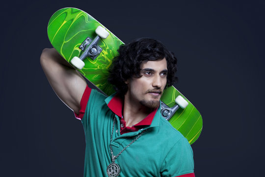 Close-up of young man holding skateboard behind head against black background 