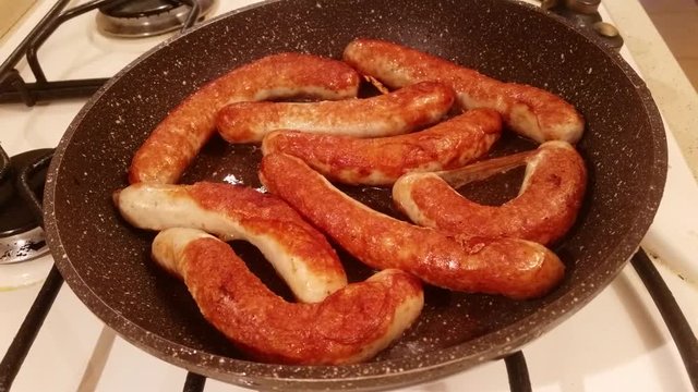 Appetizing ruddy juicy sausages fried in a large frying pan