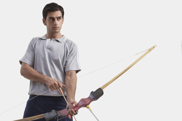 Young male archer with bow and arrow against gray background