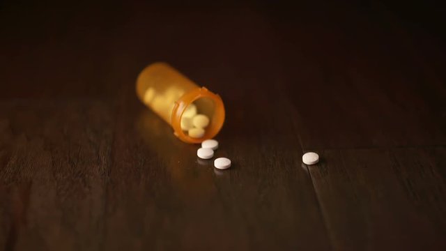 Orange Pill Bottle Falls and Some Pills Fall Out. a prescription orange bottle falls and some white pills spill out of the opening on a wooden surface. Slow motion
