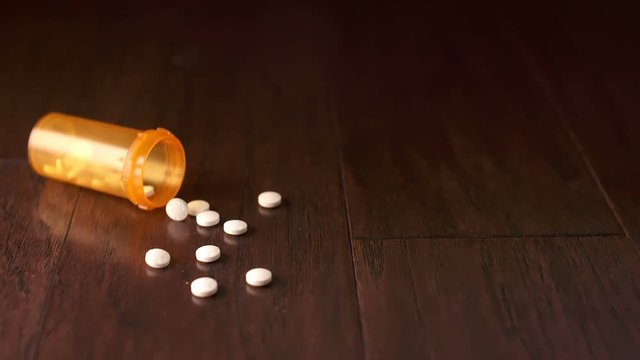 Orange Pill Bottle Falls on Left Side Slow Motion. a prescription orange bottle falls on the left side and some white pills spill out of the opening on a wooden surface. Slow motion
