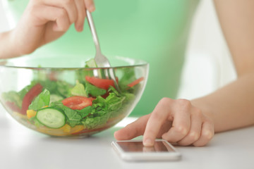 Obraz na płótnie Canvas Young woman using mobile phone for counting calories while eating salad, closeup. Weight loss concept