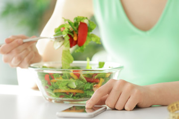 Young woman using mobile phone for counting calories while eating salad, closeup. Weight loss concept