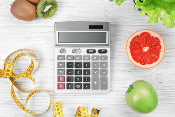 Diet concept. Calculator, measuring tape and different groceries on wooden background