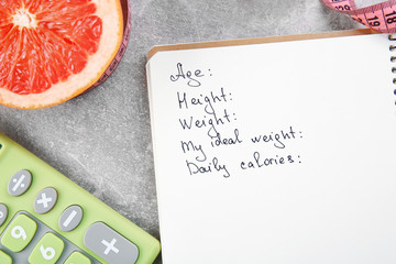 Diet concept. Calculator, grapefruit and notebook on gray background